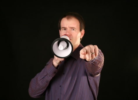 a man makes his demands known by speaking loudly through a megaphone and pointing his finger directly at YOU THE VIEWER with focus on his finger and hand
